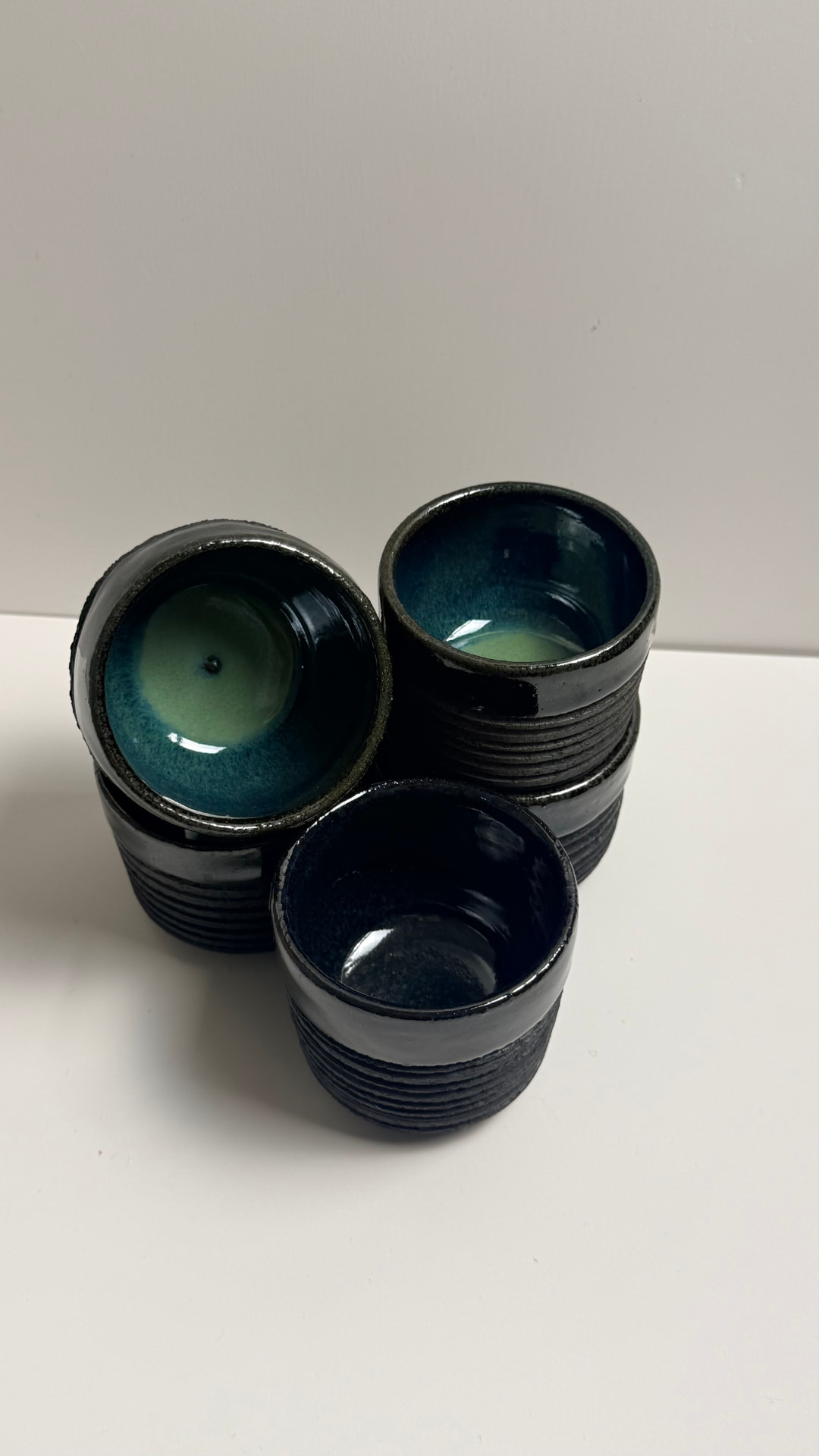Hand-thrown espresso cups with a raw, unglazed clay exterior and a glossy black rim, interiors glazed from Oribe green to indigo