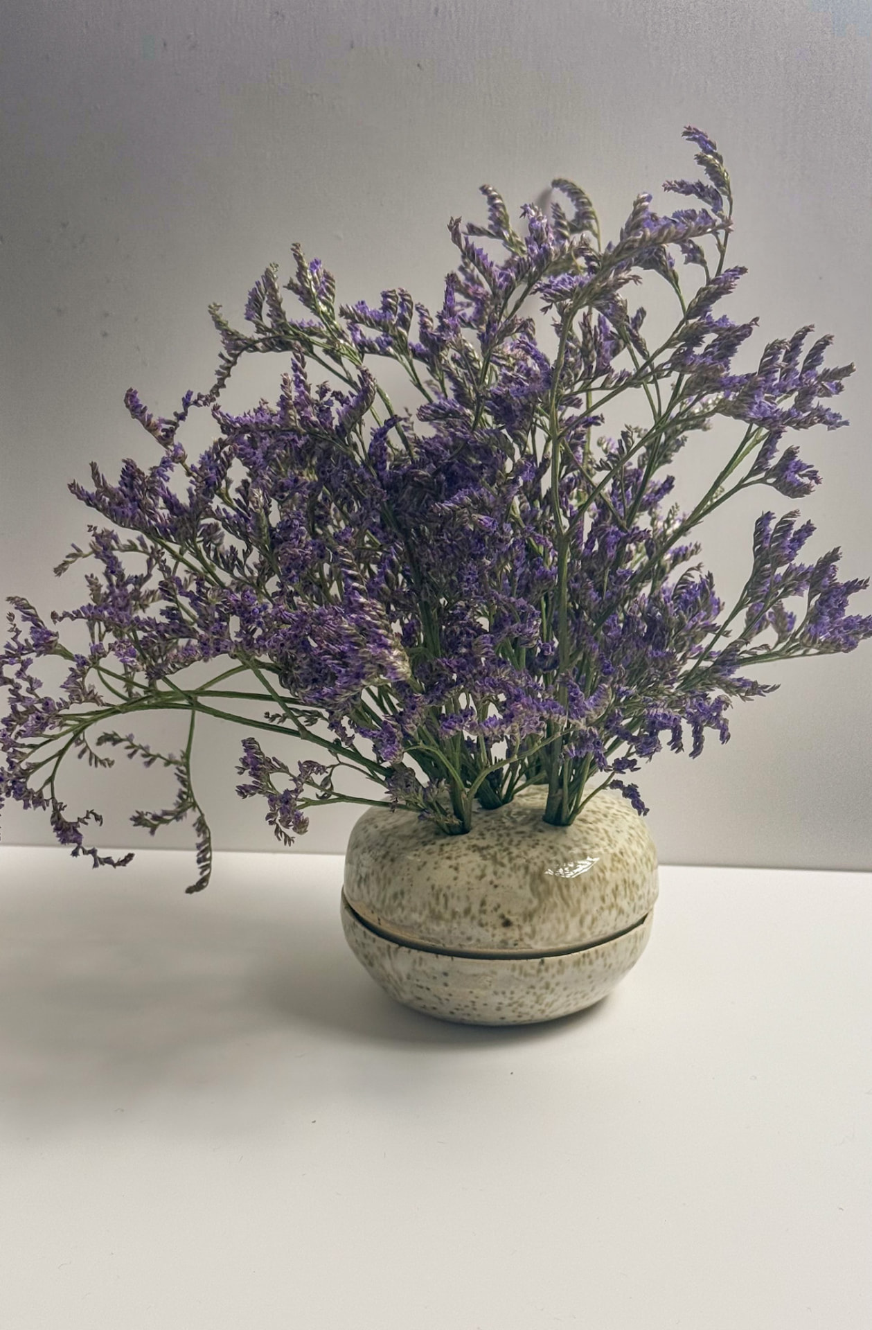 A rounded, two-piece bud vase in a speckled green glaze, the top lifted off the base