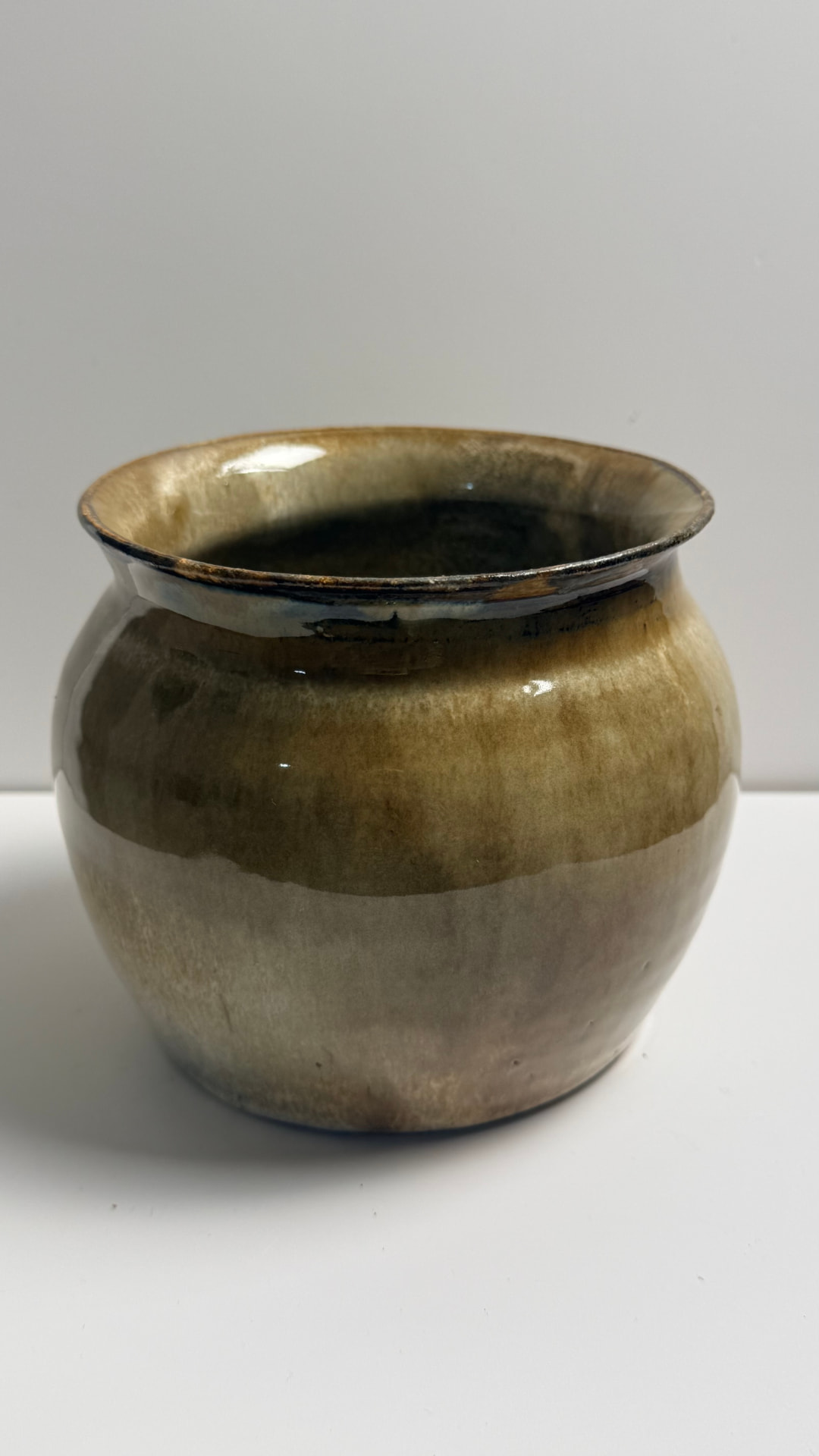 A rounded, full-bodied vase with a narrow flared rim, glazed in warm earthy tones from sandy beige to deep olive